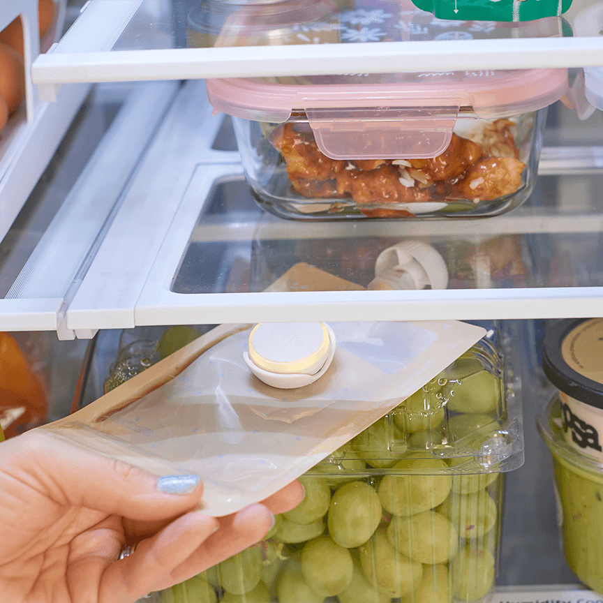Photo of woman reaching into fridge and grabbing a baby food pouch with Ovie LightTag lit yellow on the to pof it.