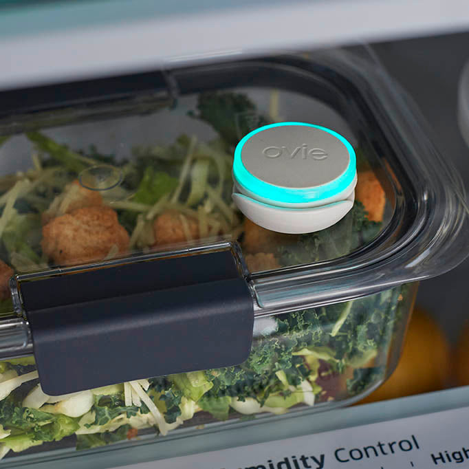 Close up of Ovie LightTag lit teal on top of clear food storage container with salad inside