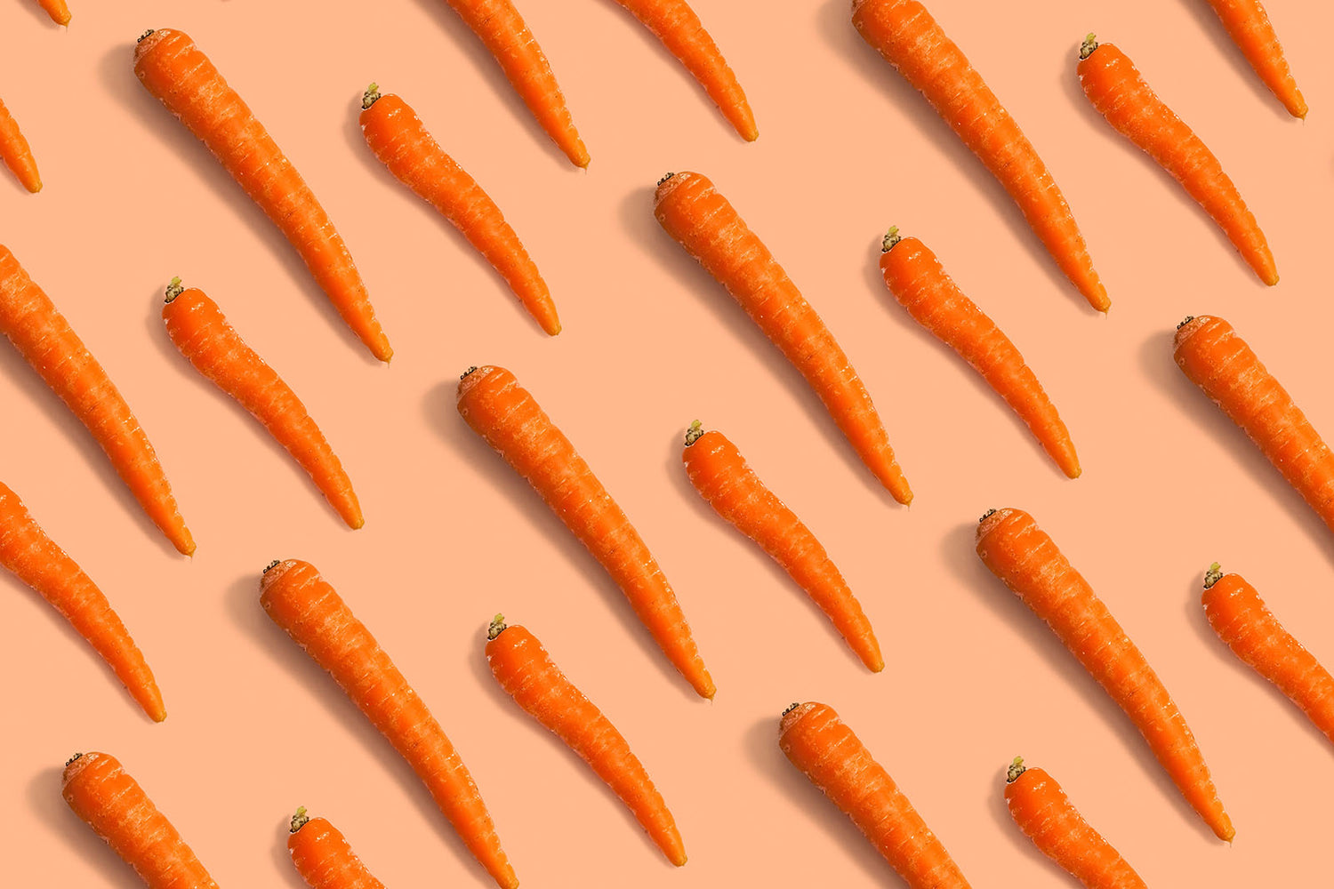 Bright, fun image from above of orange carrots laid out in diagonal pattern on a light orange background