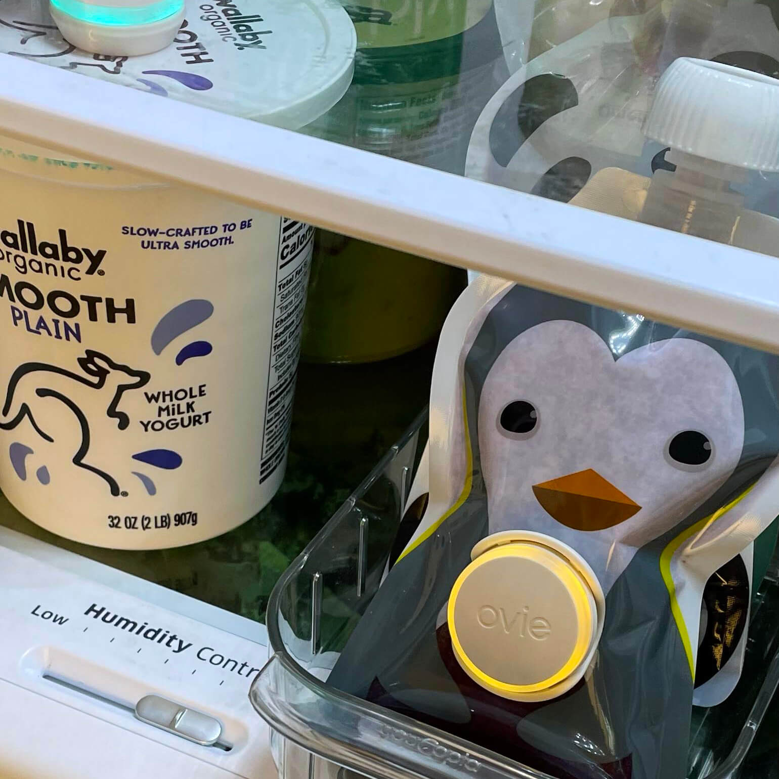 Closeup of cute penguin-shaped food pouch with smoothie inside. Pouch has Ovie LightTag on the front that is lit up yellow.