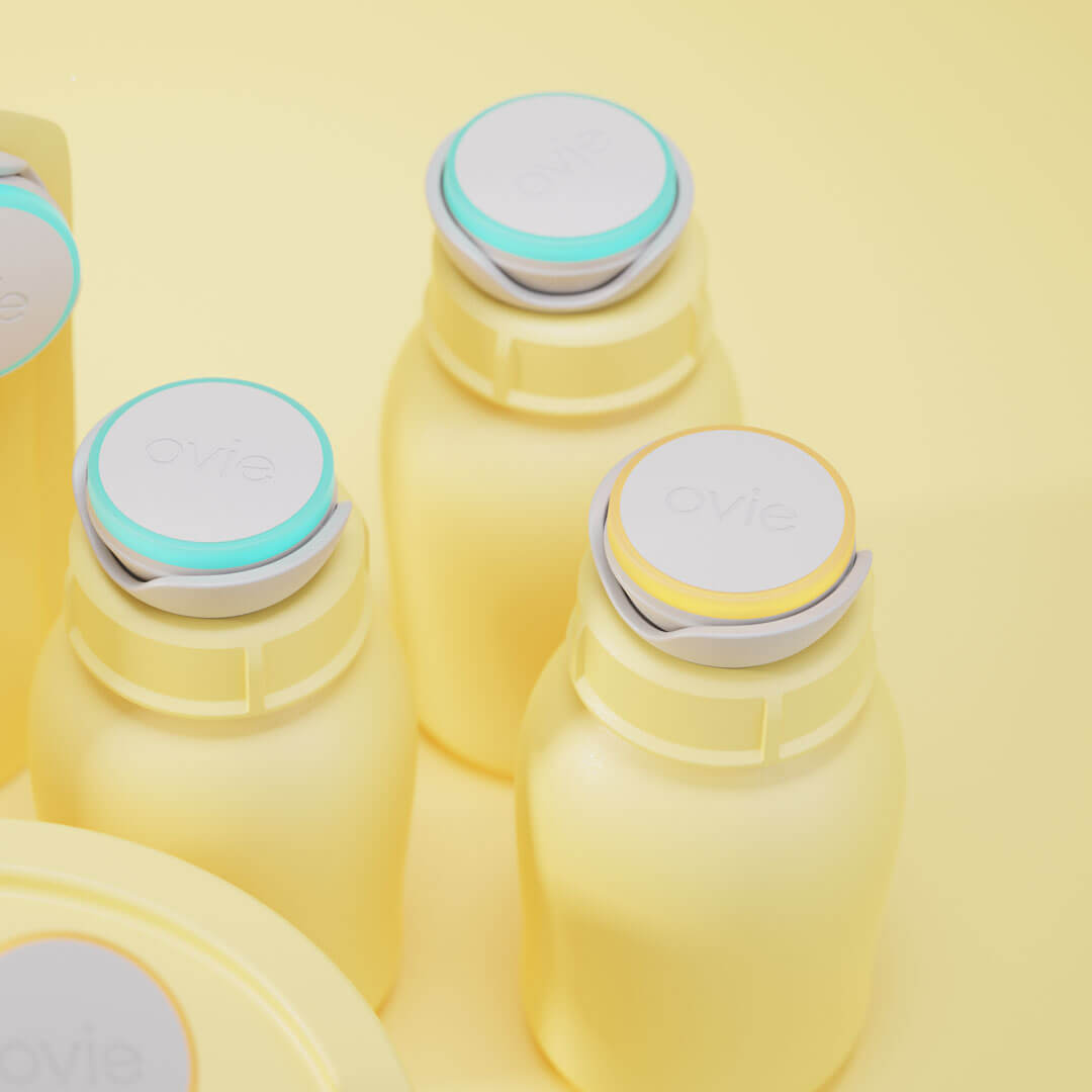 Close up image of 3 lit-up Ovie LightTags on baby milk bottle lids. Bottles and entire background are colored pale yellow