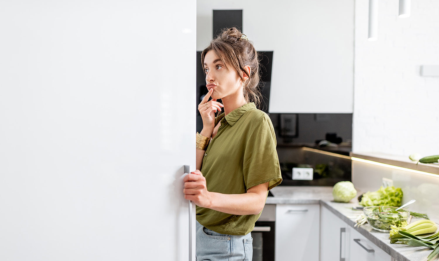 Photo of woman standing in all white kitchen looking skeptically into an open refrigerator