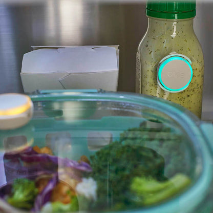 Closeup photo in fridge showing dressing container in back of fridge with a lit up Ovie LightTag that is glowing.