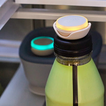 Closeup photo of Ovie LightTag lit yellow on to pof drink bottle. Blurred out food container with teal light tag can be seen in the background of the photo