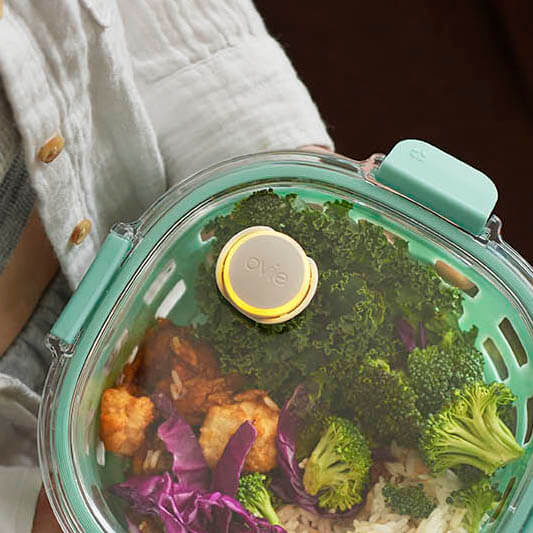 Photo of hip young woman holding beautiful food in cool ello container with Ovie LightTag lit yellow on top. 