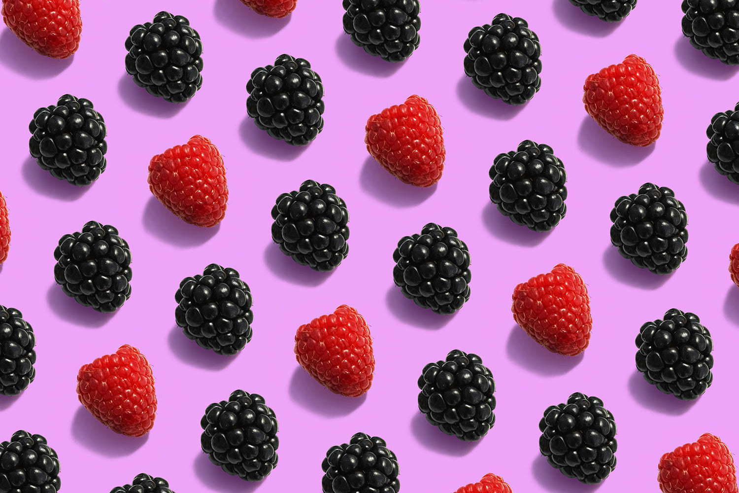Bright stylized image with blackberries and raspberries arranged in a pattern that fills the image on a bright fuchsia background
