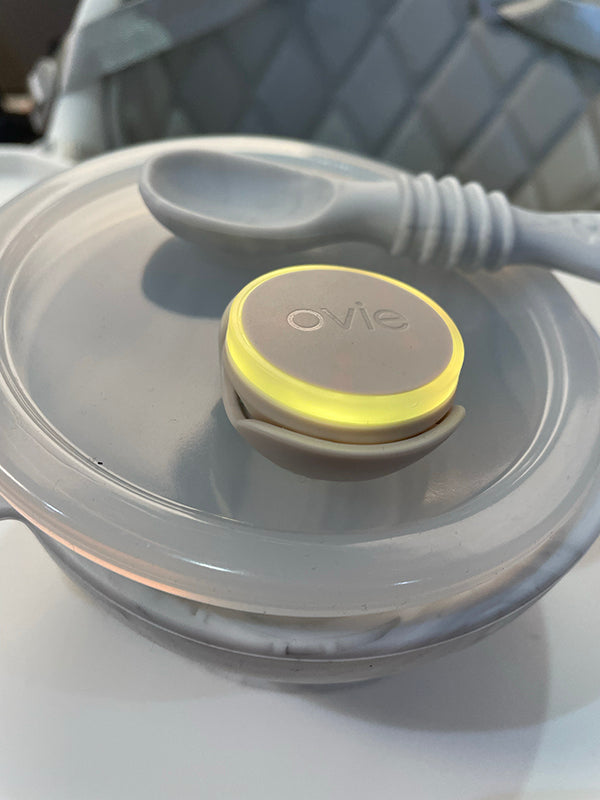 Photo of Ovie LightTag lit up yellow on top of modern gray baby food container on high chair